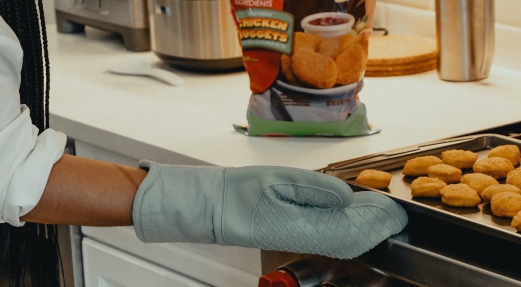 A woman taking cookies out of the oven with oven mitts