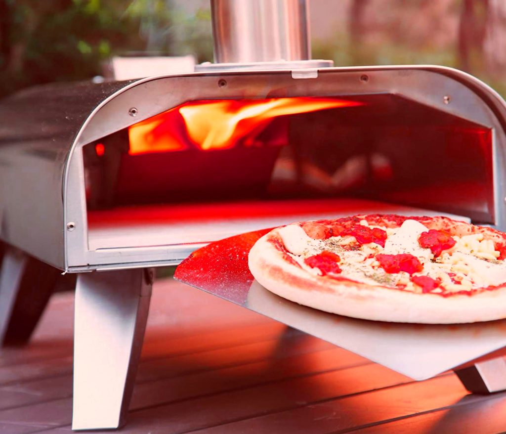 A compact lightweight portable pizza oven placed on a table cooking a pizza.